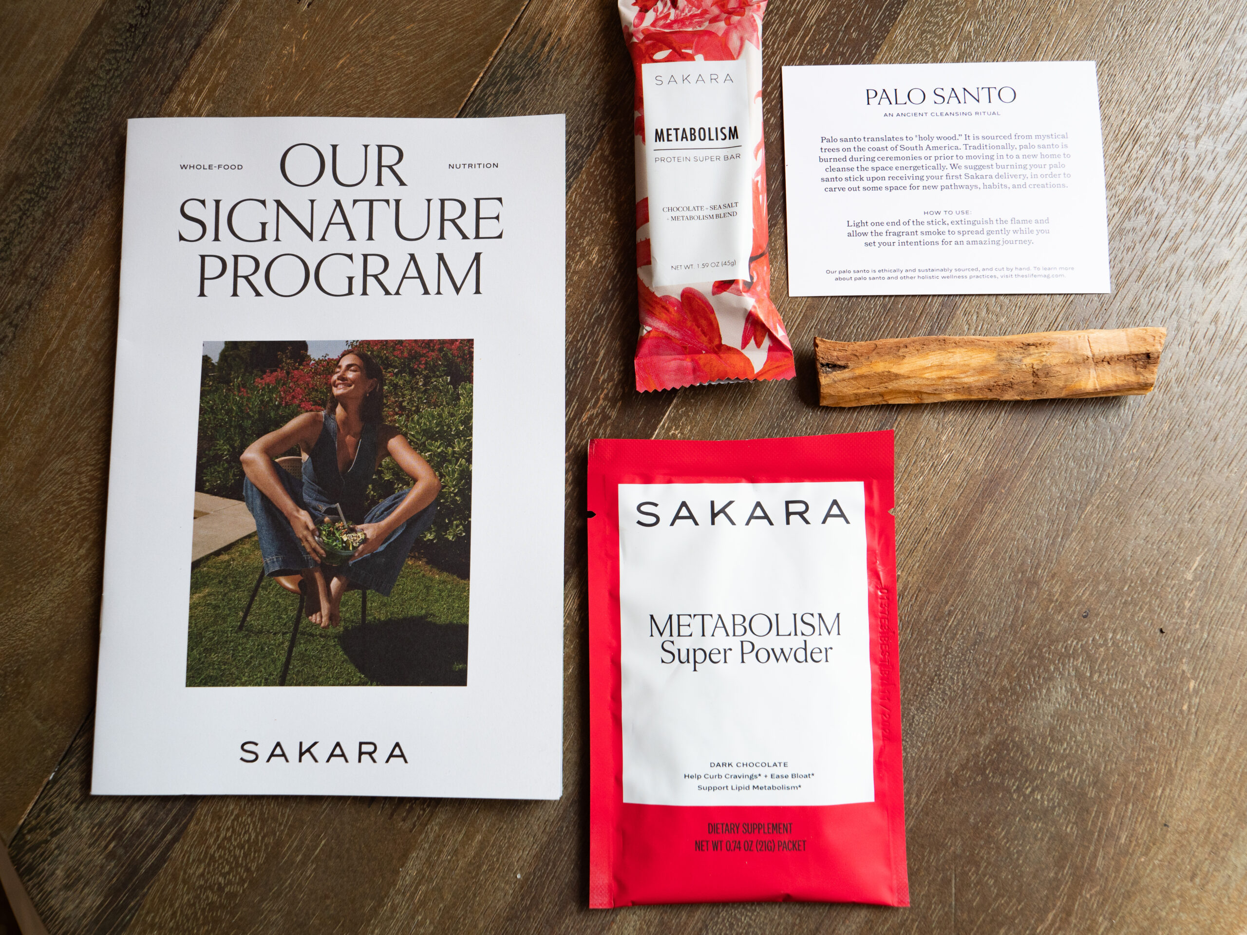 A laid-out display includes a program booklet titled "Our Signature Program," a sachet of Metabolism Super Powder, a bar labeled Metabolism, and a Palo Santo stick with its description card.