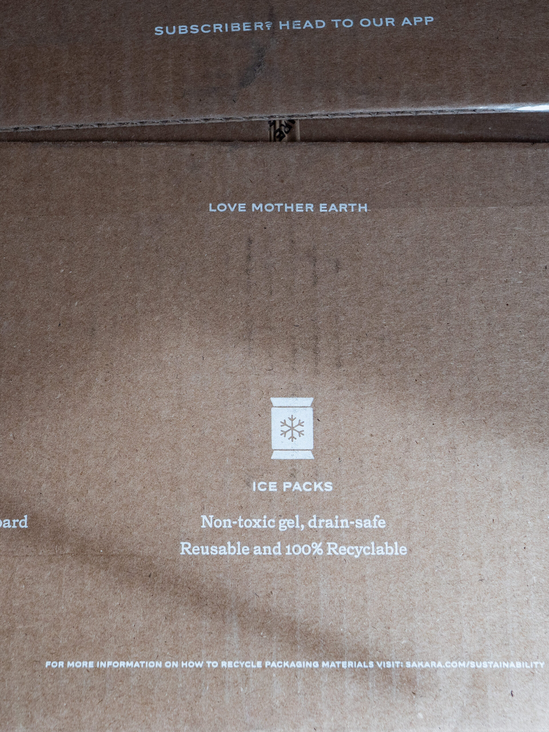 A cardboard box with text detailing recycling information: 100% recyclable cardboard, non-toxic and reusable ice packs, and meal containers made from repurposed plastic bottles.