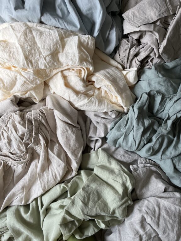 A pile of crumpled sheets and fabric in various colors, including beige, green, blue, and gray.
