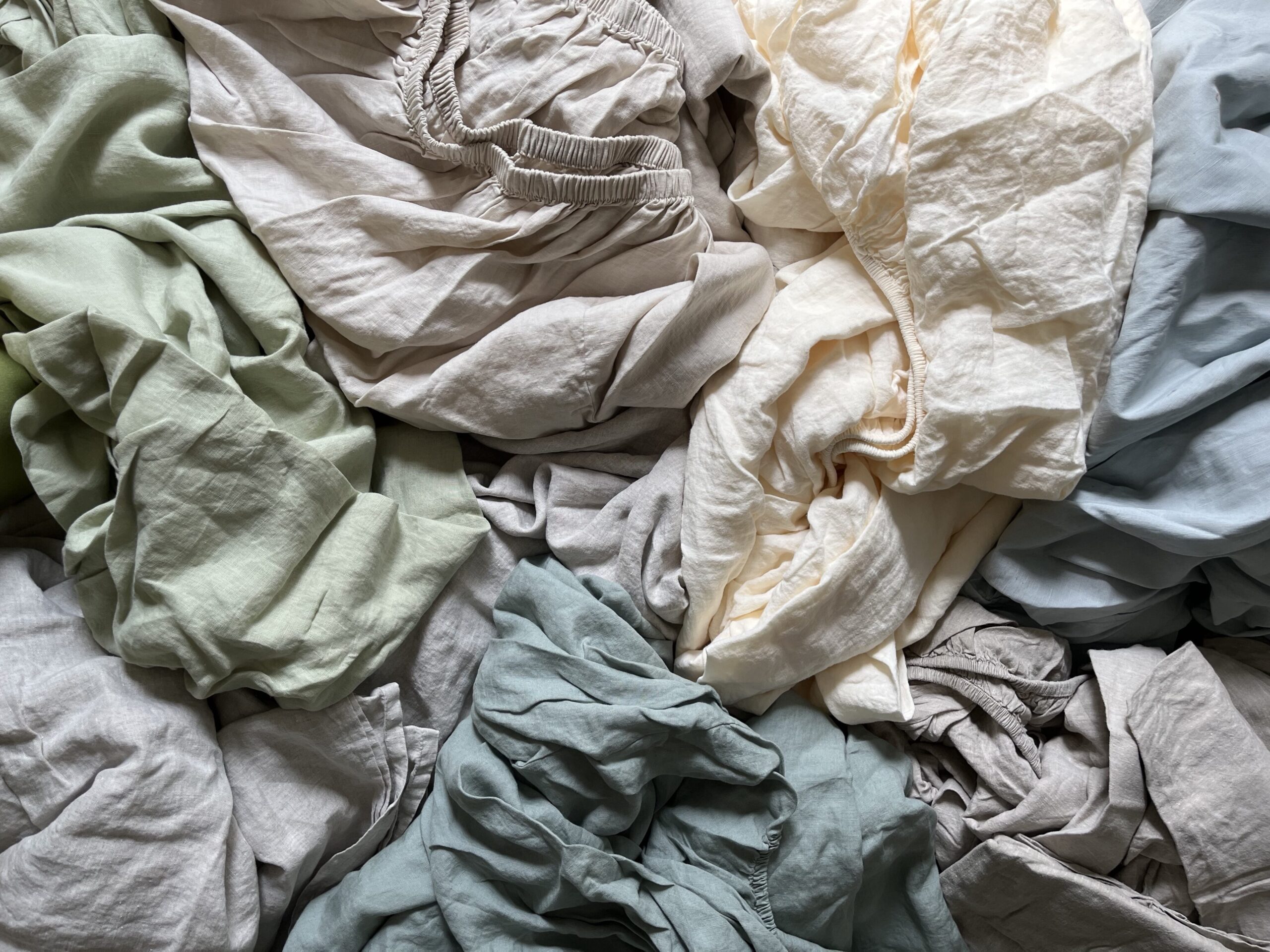 A pile of crumpled sheets and fabric in various colors, including beige, green, blue, and gray.