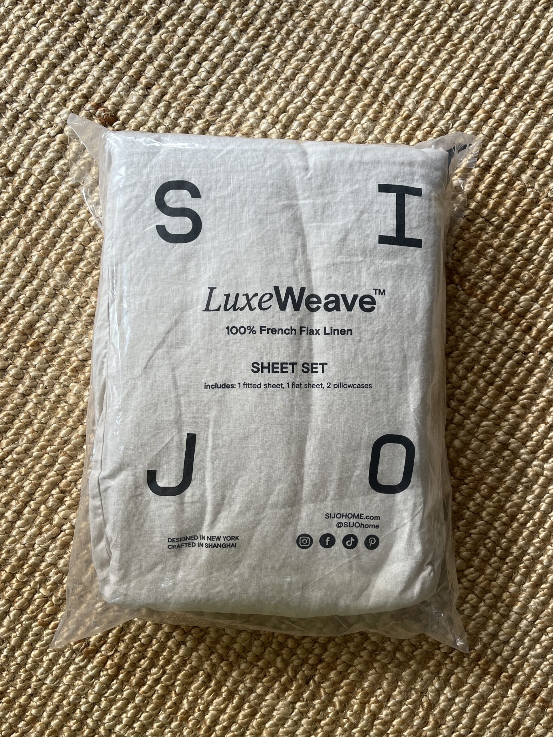 A packaged LuxeWeave sheet set labeled as 100% French Flax Linen, including 1 fitted sheet, 1 flat sheet, and 2 pillowcases, rests on a textured surface.