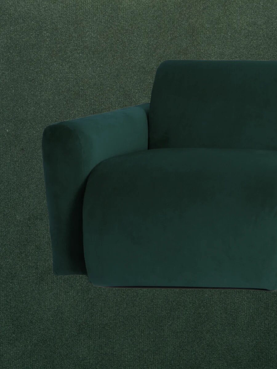 Green velvet sofa with one armrest, photographed against a matching green background.