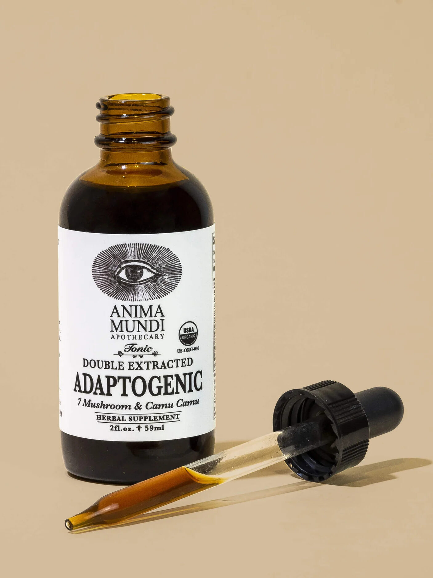 A brown bottle labeled "Anima Mundi Apothecary Tonic" with "Double Extracted Adaptogenic" and "7 Mushrooms & Camu Camu". The dropper is placed in front of the bottle, filled with a brown liquid.