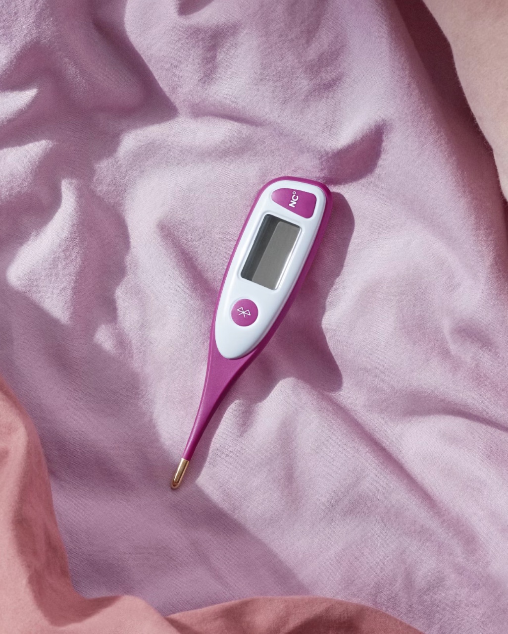 Digital thermometer with a pink and white design resting on a pink fabric surface.