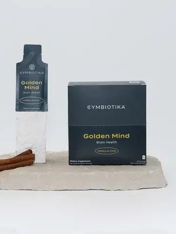 Cymbiotika Golden Mind Brain Health Vanilla Chai supplement package with a sachet and cinnamon sticks displayed on a stone surface against a white background.