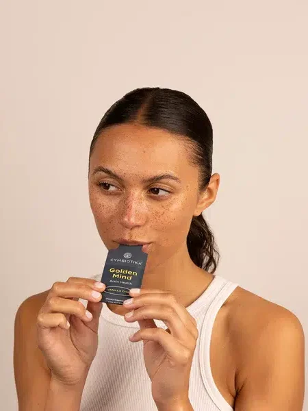 A person with tied-back hair holds a small, rectangular product labeled "Golden Mind" close to their mouth while wearing a white sleeveless shirt.