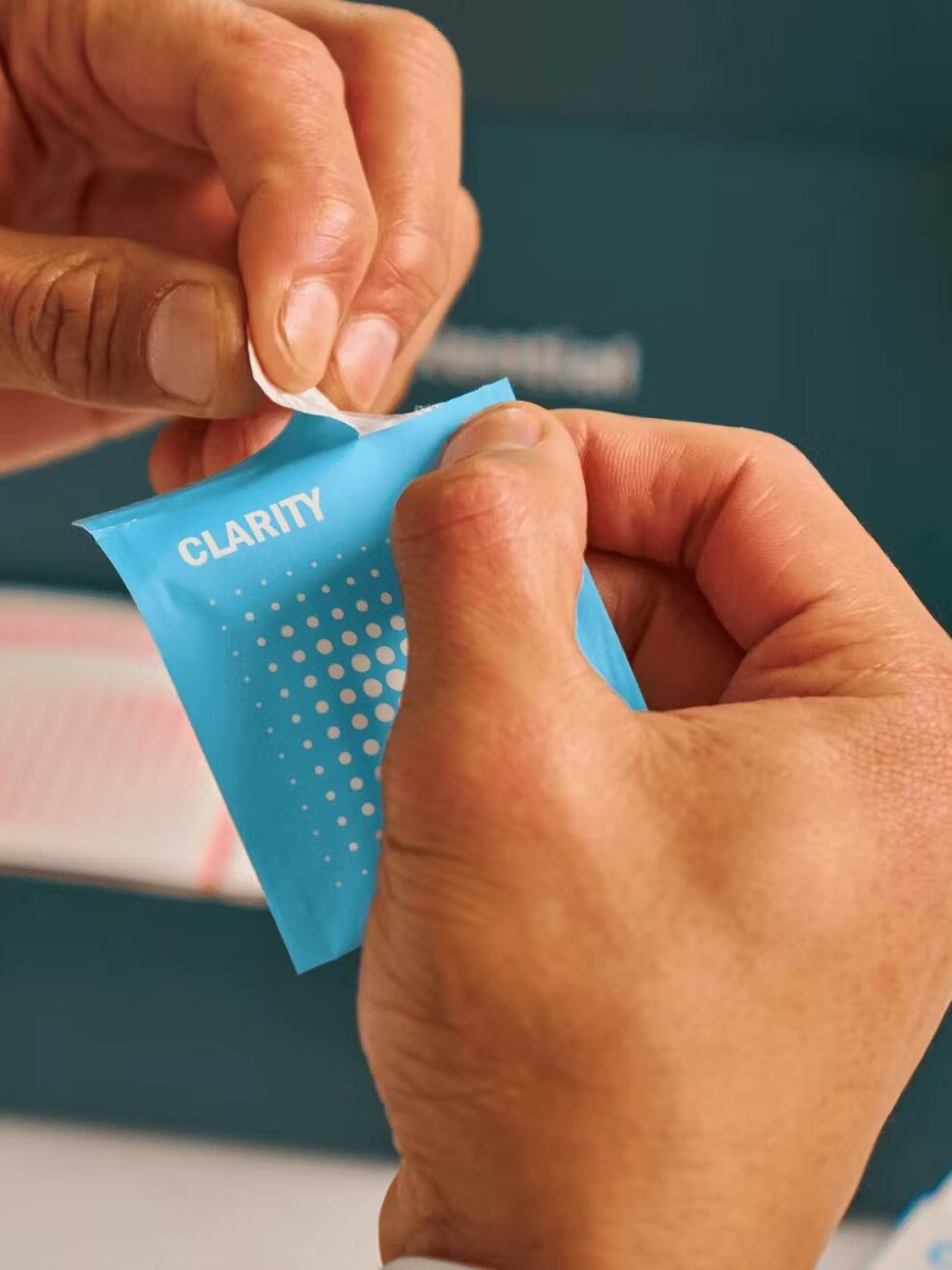 A person opens a small blue packet labeled "CLARITY.