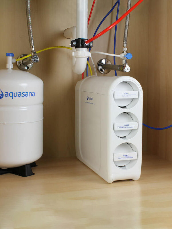 Under-sink water filtration system showing a water filter unit with three labeled cartridges, connected to a pressurized storage tank on the left and additional tubing.