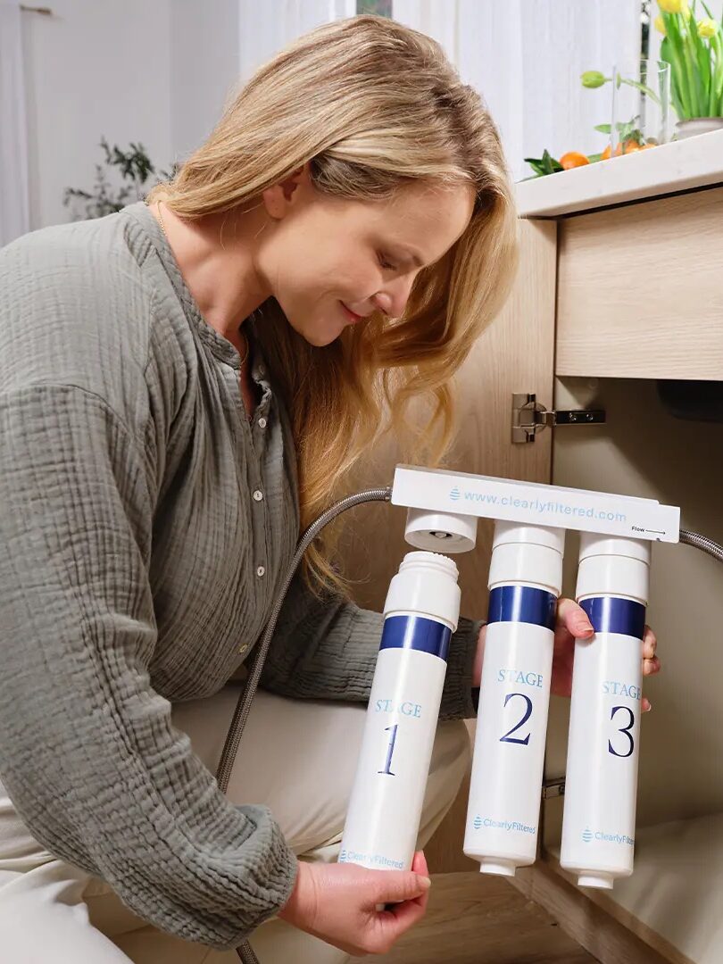 Person installing a three-stage water filtration system under a sink.