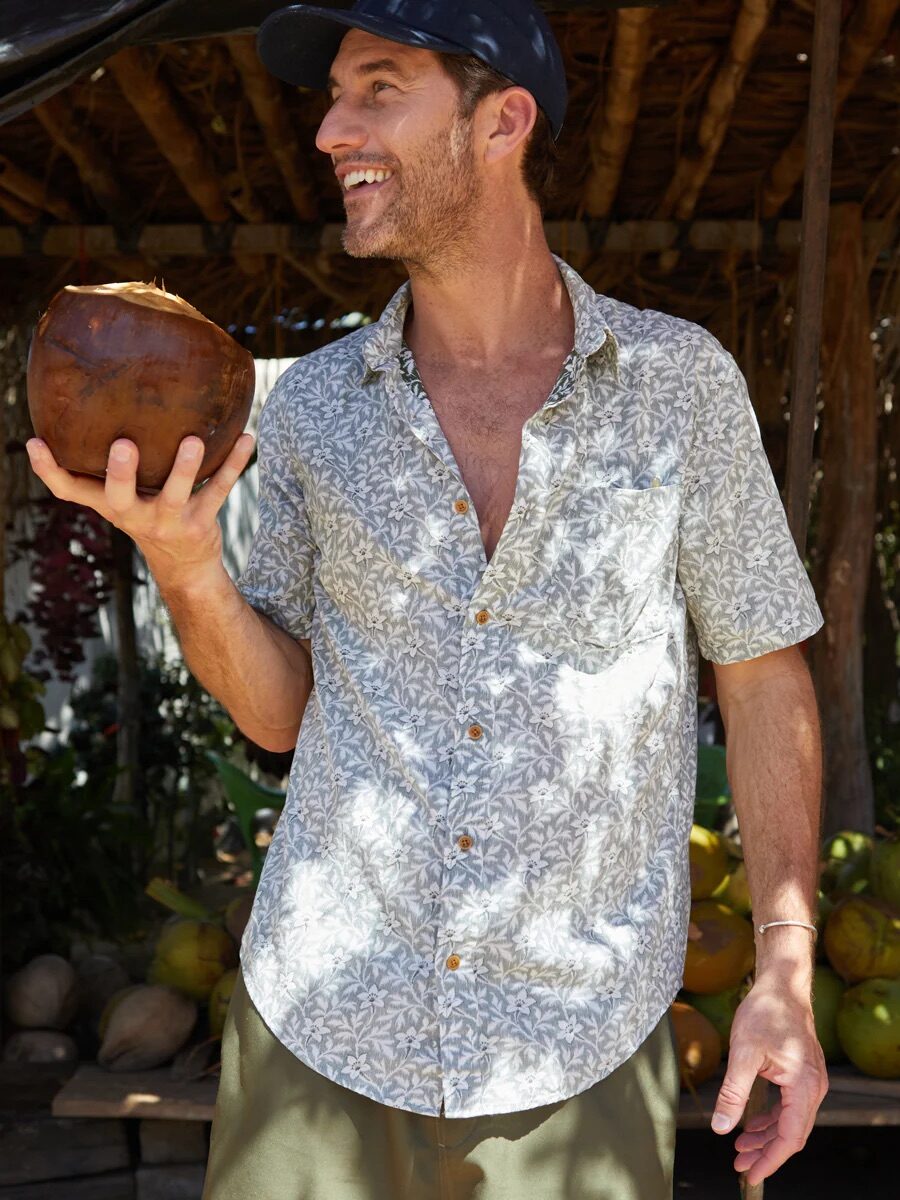 A model wearing a button down collared short sleeve in a blue and white floral pattern from Outerknown. 