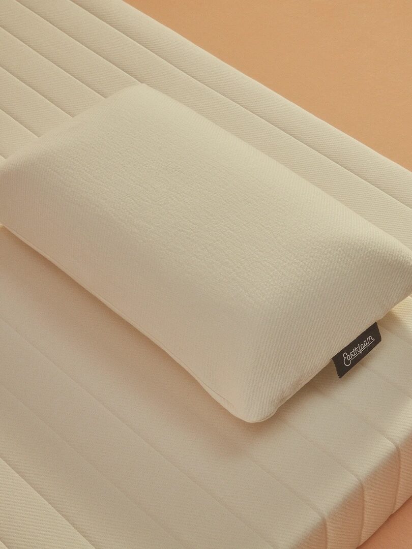 A cream-colored pillow is placed on a matching cream-colored mattress with a textured surface and a tag attached to the pillow.