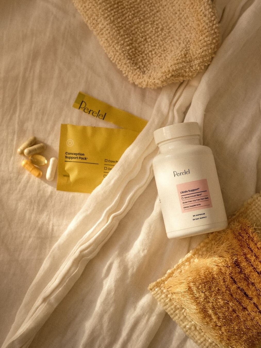 A bottle of "Peretel" supplements and two yellow packets are on a beige fabric surface, alongside four pills and a textured fabric.