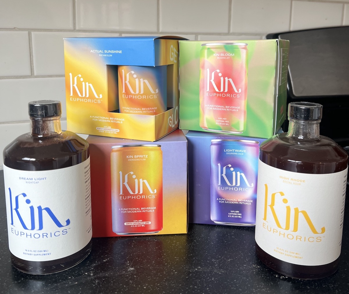 Bottles and cans of Kin Euphorics beverages, including the delightful kin drink varieties Dream Light, Actual Sunshine, Kin Spritz, Kin Bloom, Lightwave, and High Rhode, are beautifully arranged on a kitchen counter.