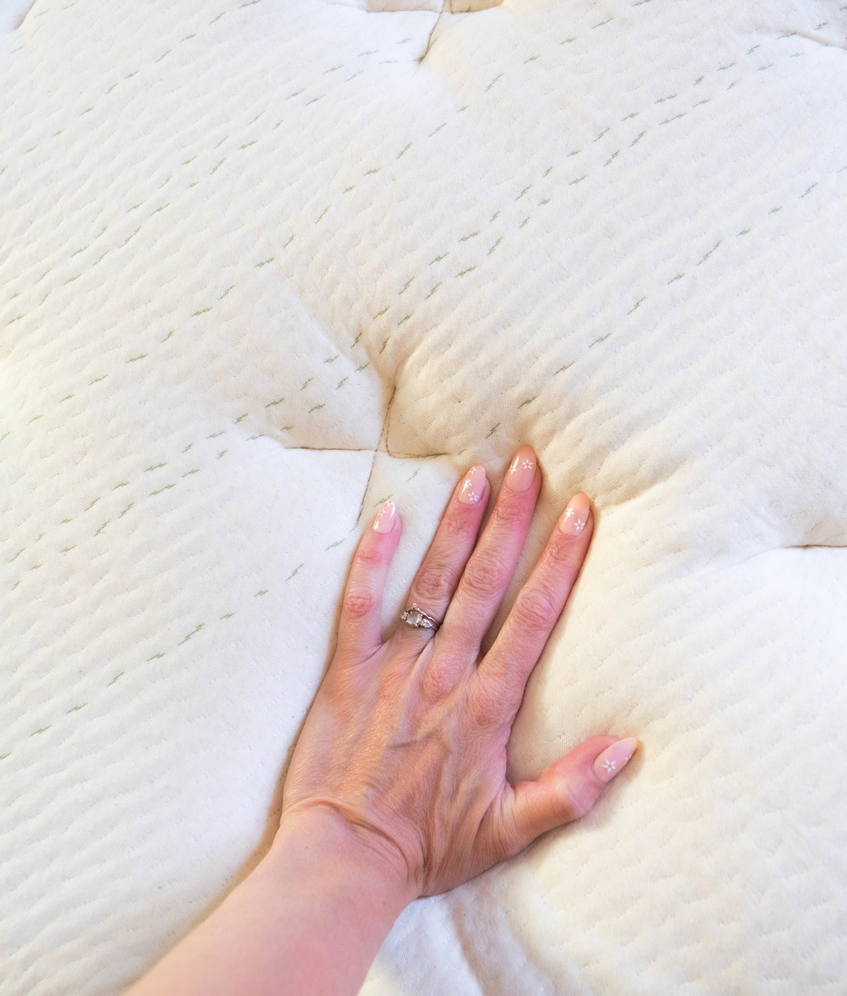 A hand pressing down on a soft, quilted organic mattress, showcasing its texture and cushioning.