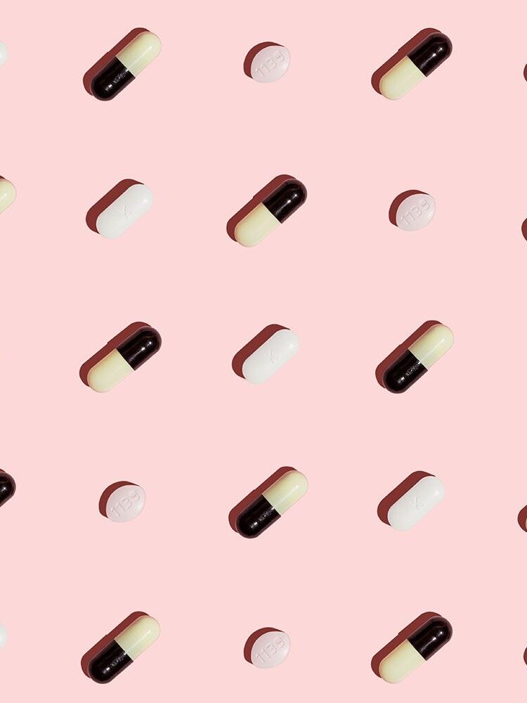 A pattern of black and white capsules and white round tablets evenly spaced on a pink background.