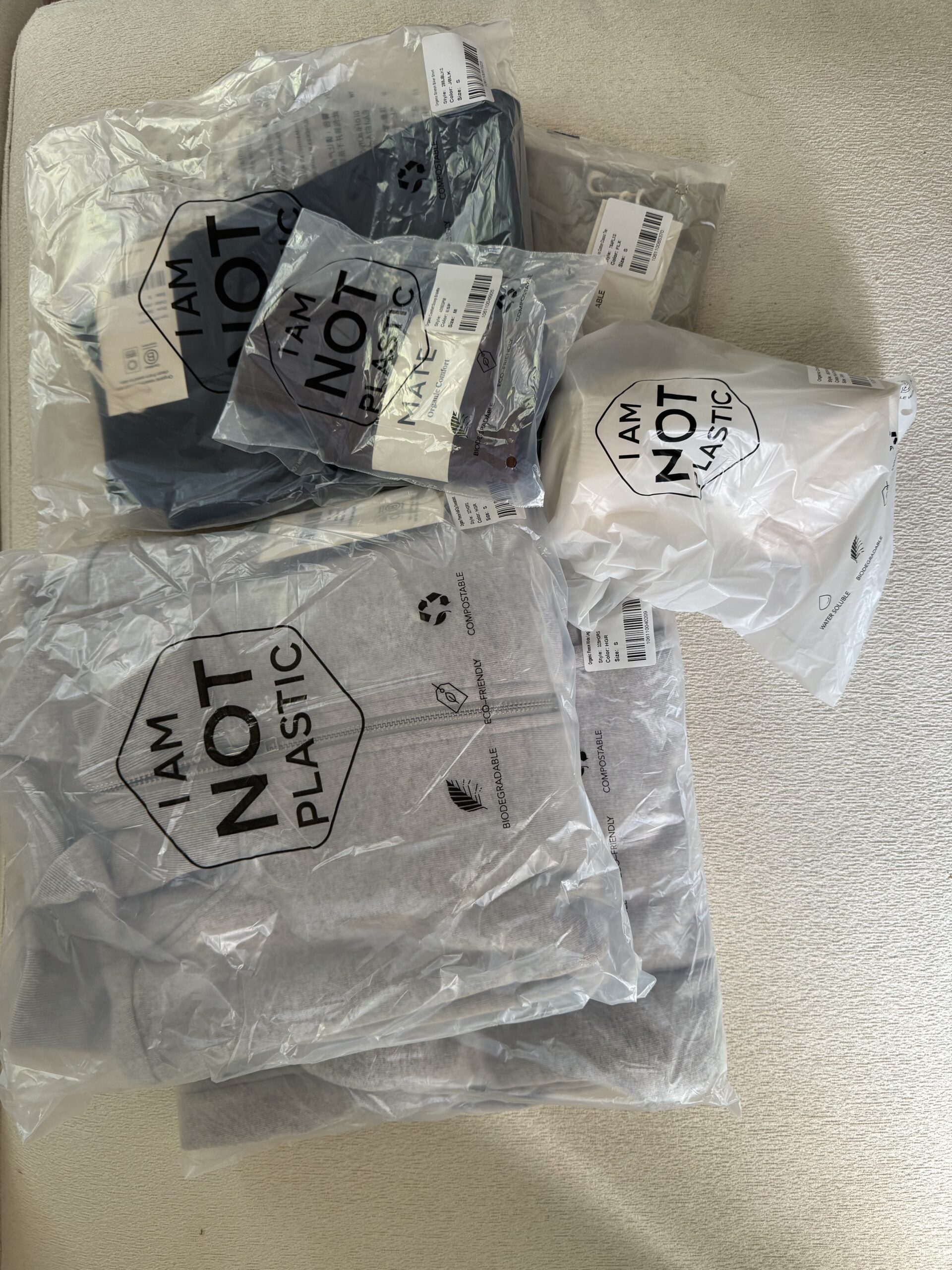 Plastic packages labeled "I am not plastic," containing various folded clothing items, are arranged on a light-colored surface.