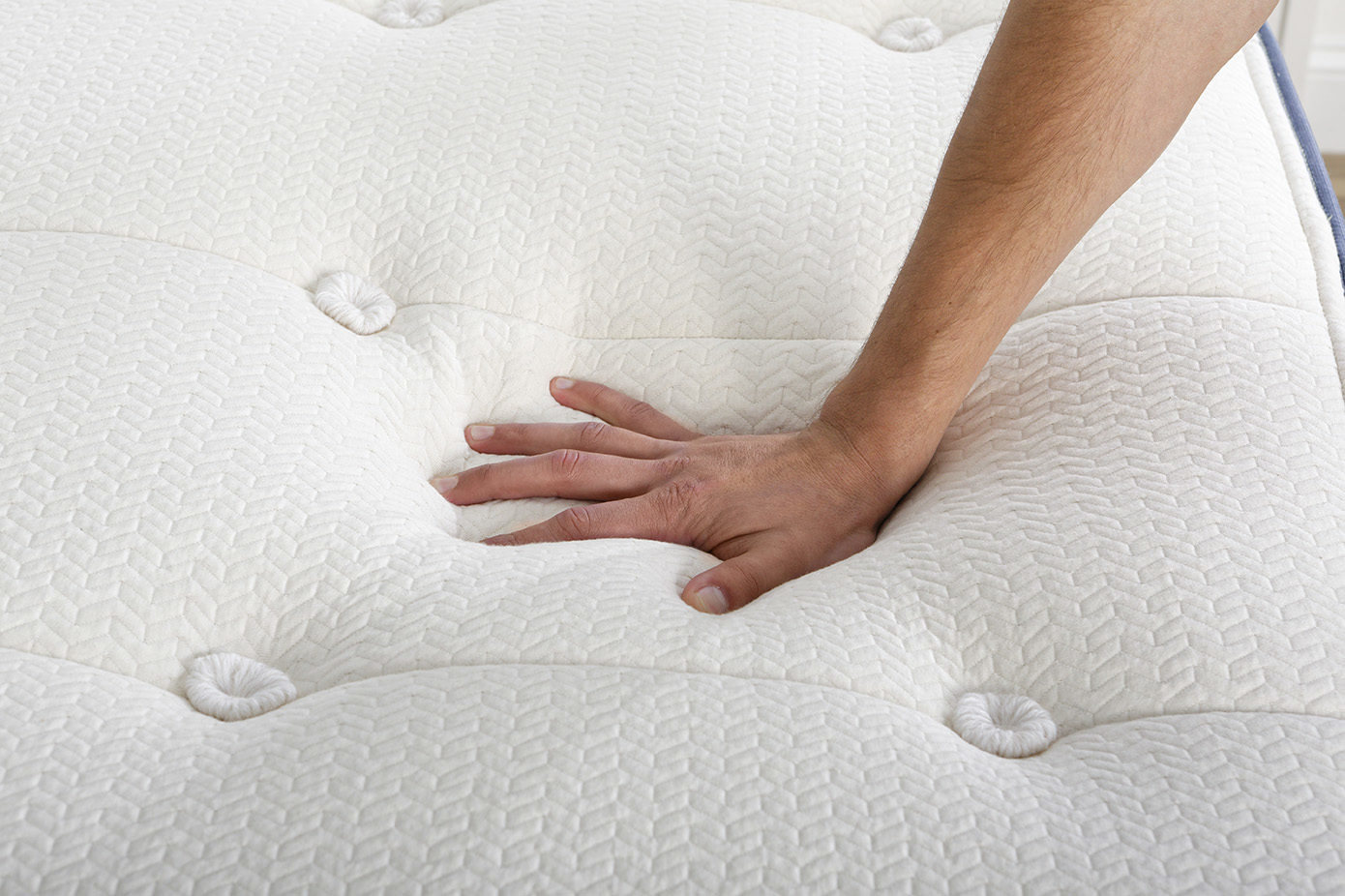 A hand presses down on a white, tufted organic mattress, showcasing its cushioning and softness.