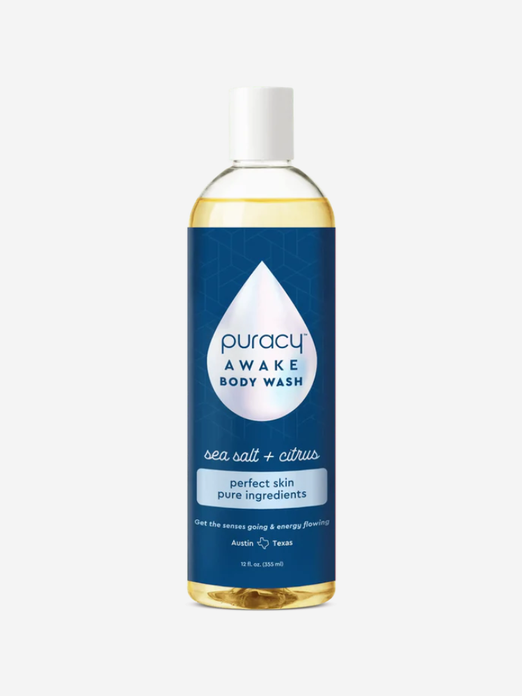 A bottle of Puracy Awake Body Wash with sea salt and citrus, labeled with text stating "perfect skin pure ingredients" and "Get the senses going & energy flowing." The bottle contains 18 fl oz.