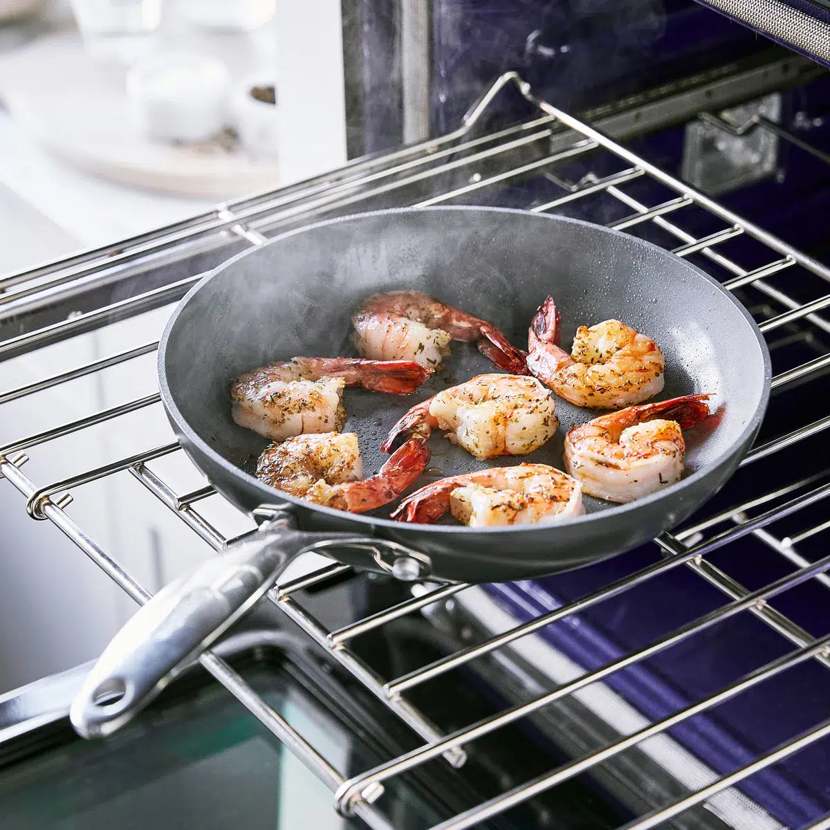 Shrimp cooking in a frying pan on an oven rack, with steam rising.
