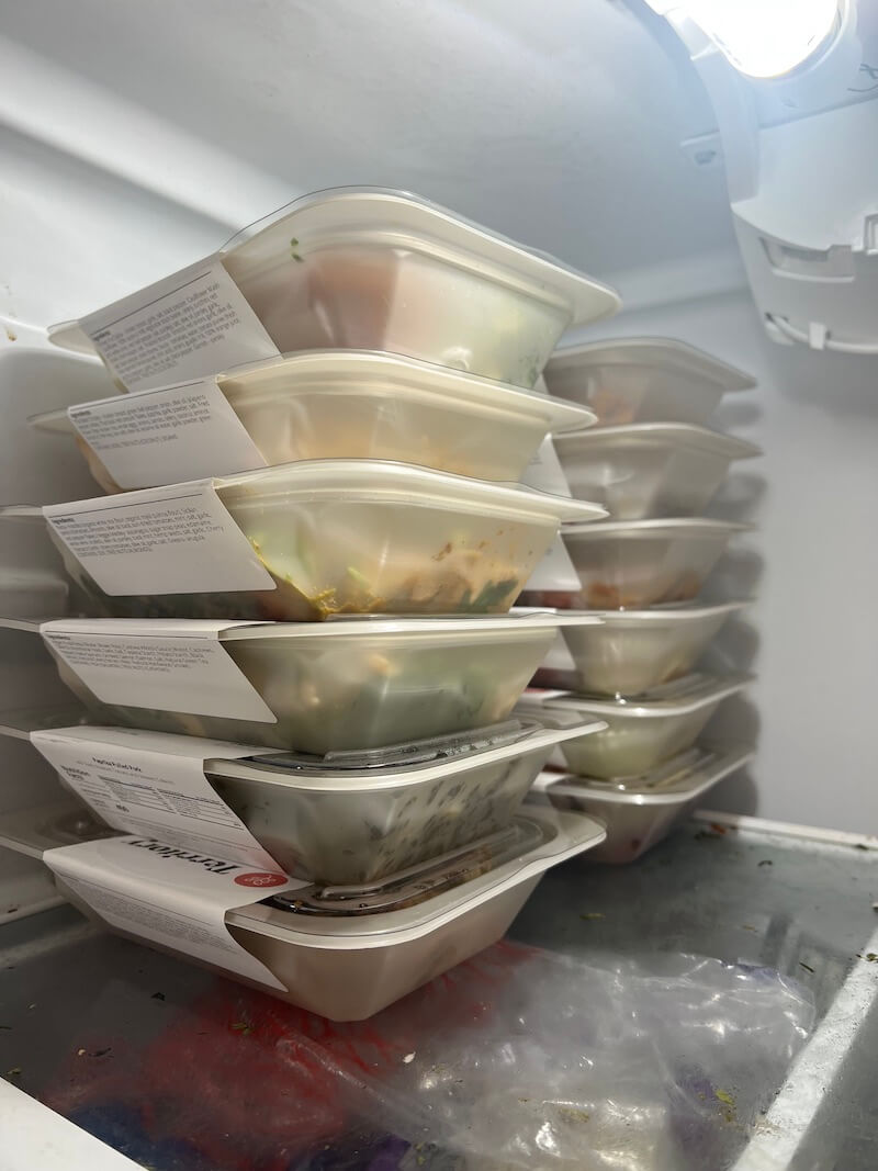 Stacked plastic containers filled with various meals are arranged inside a refrigerator.