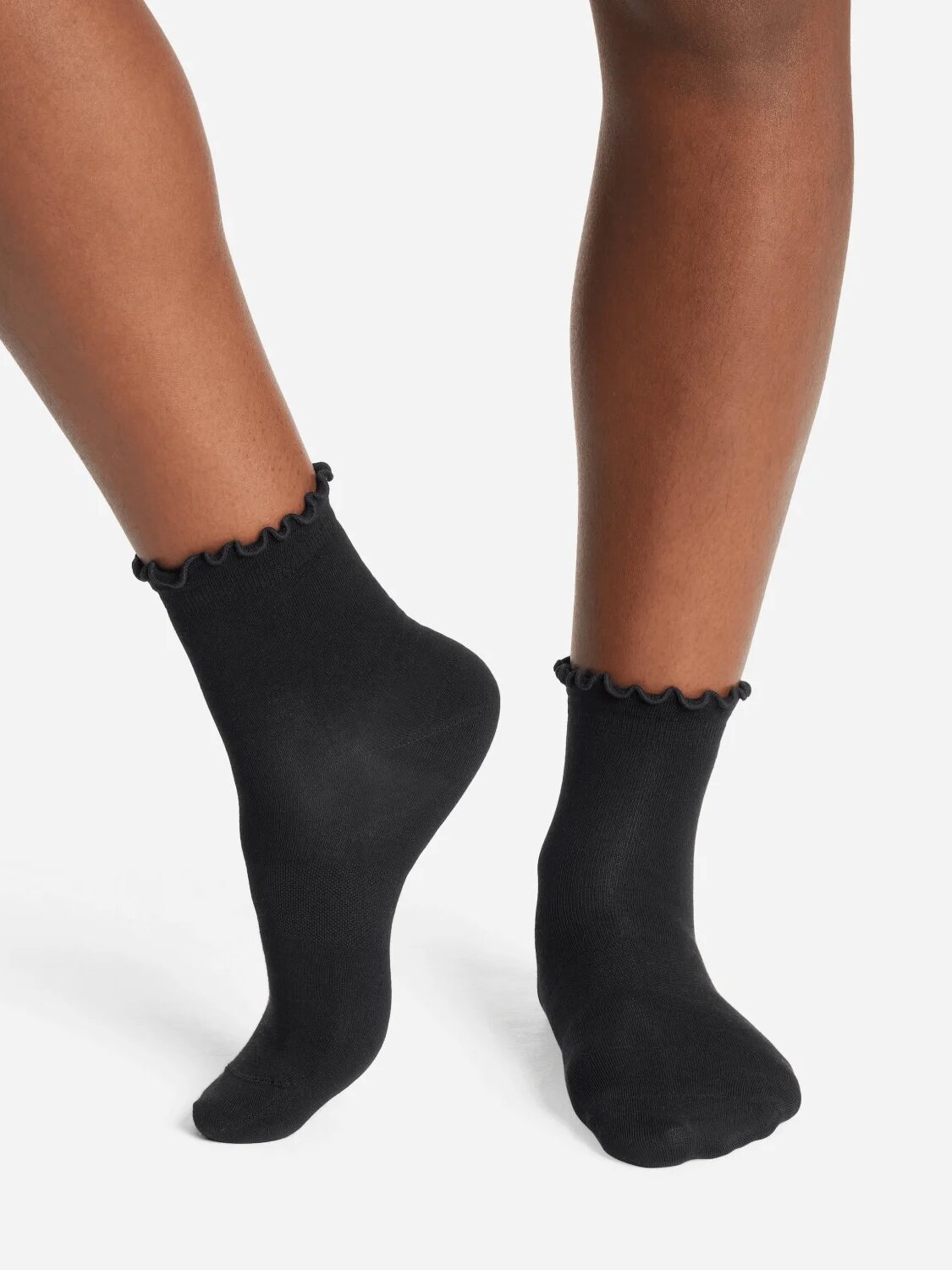 A pair of feet wearing black ruffled organic socks is shown against a plain white background.