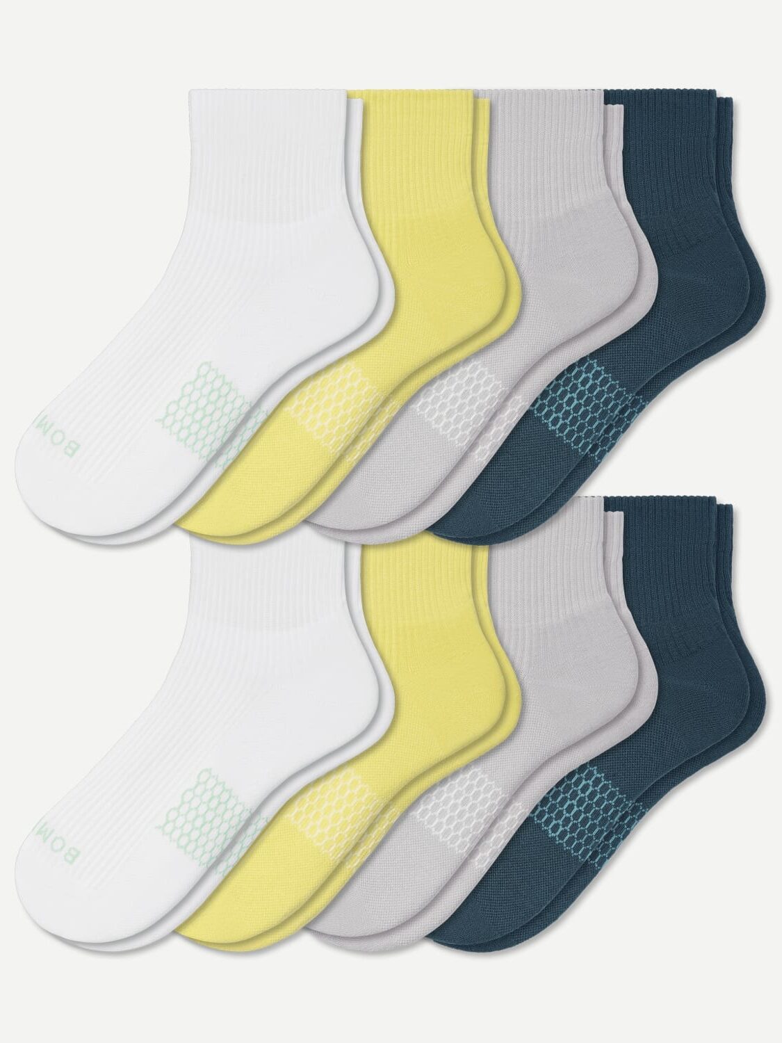 A set of eight pairs of unisex organic socks in white, yellow, light gray, and dark blue colors arranged in two rows. Each pair features a patterned section near the arch area.