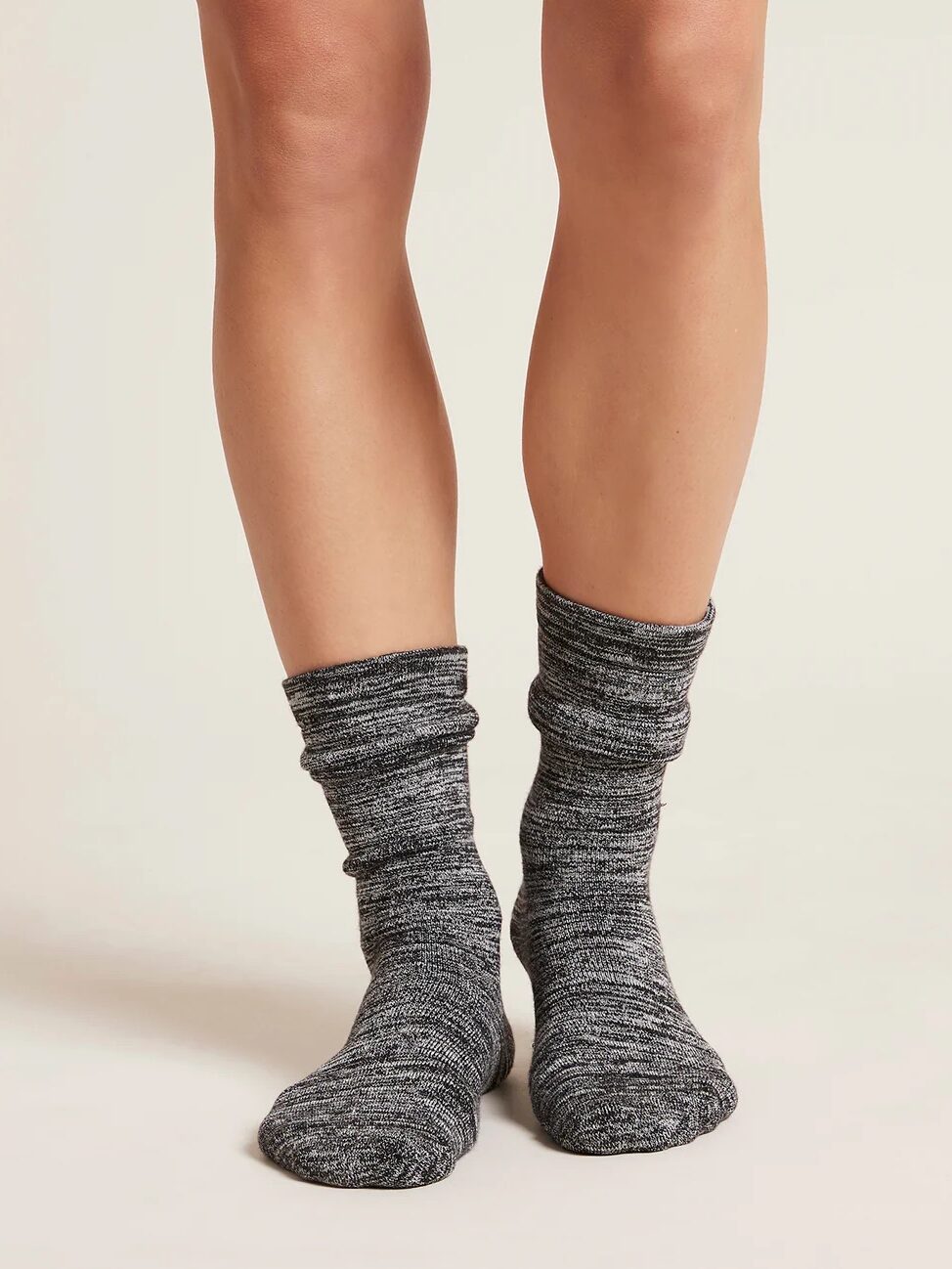 Close-up of a person wearing gray, slouchy, organic knit socks, standing on a light-colored surface.