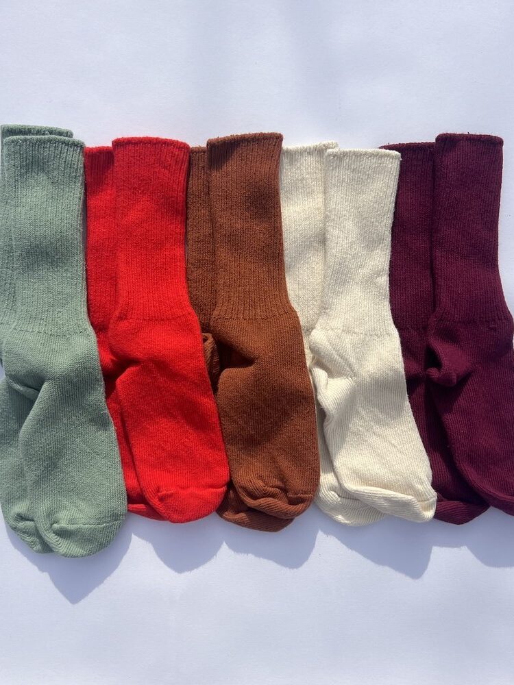 A row of six neatly arranged organic socks in different colors: green, red, brown, off-white, and dark purple, placed on a white background.