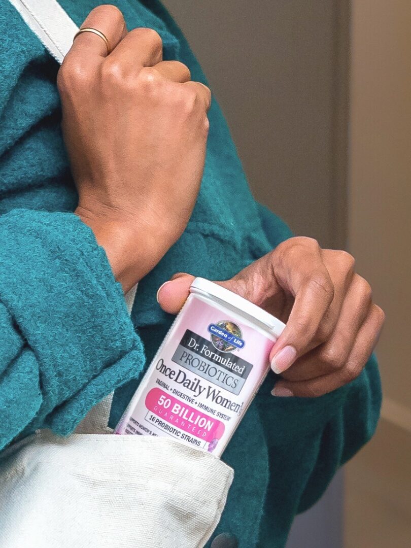 A person in a teal coat places a container of Dr. Formulated Probiotics for women into a white bag.