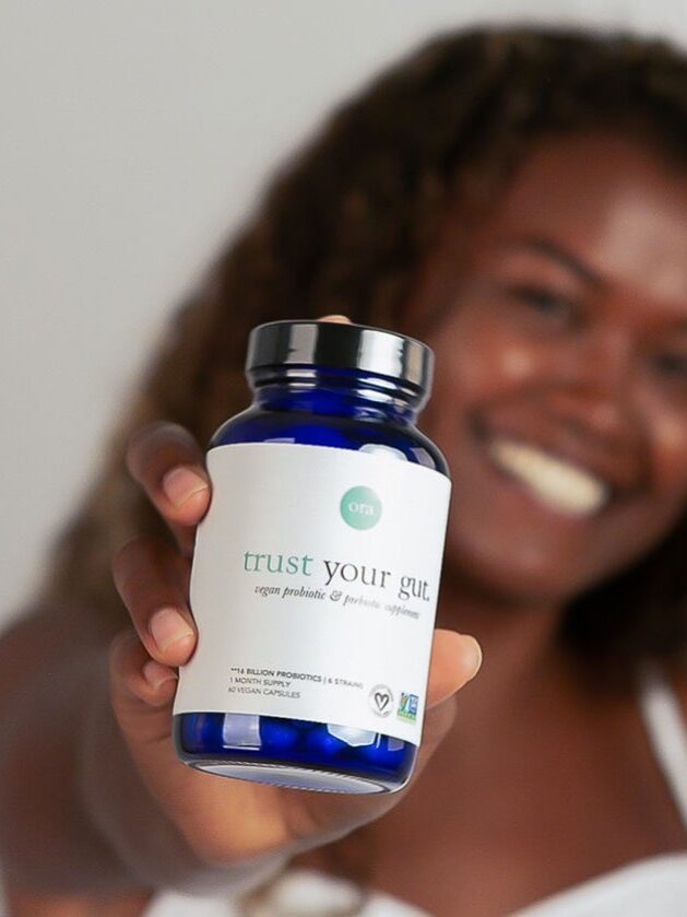 A person holding up a blue bottle labeled "trust your gut," which appears to be a supplement.