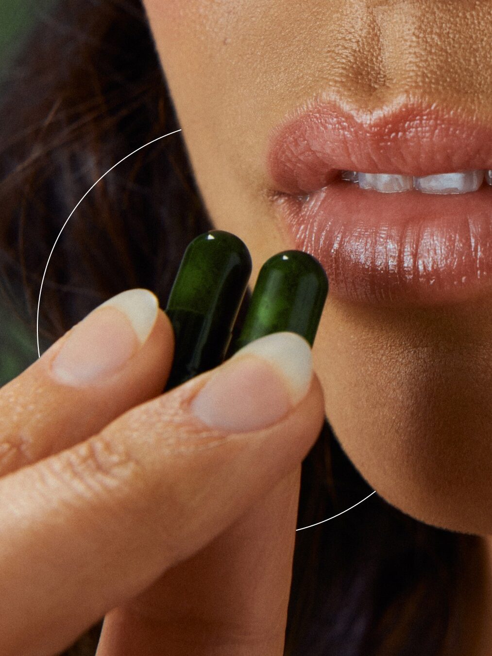 Close-up of a person holding two green capsules near their lips, about to consume them. Only the lower half of the face is visible.