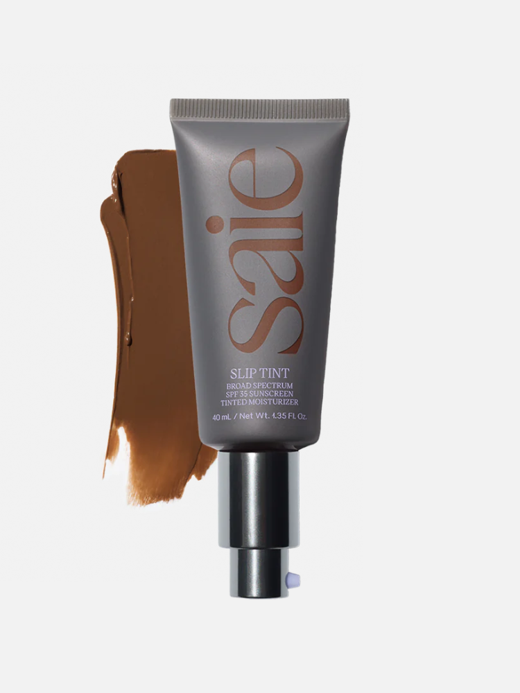 A gray tube labeled "Saie Slip Tint" stands in front of a brown smear of the tinted moisturizer. It has a pump dispenser and contains 40 ml (1.35 fl oz) of product.