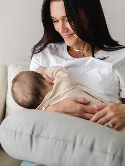 A model nurses her baby using a gray support pillow.