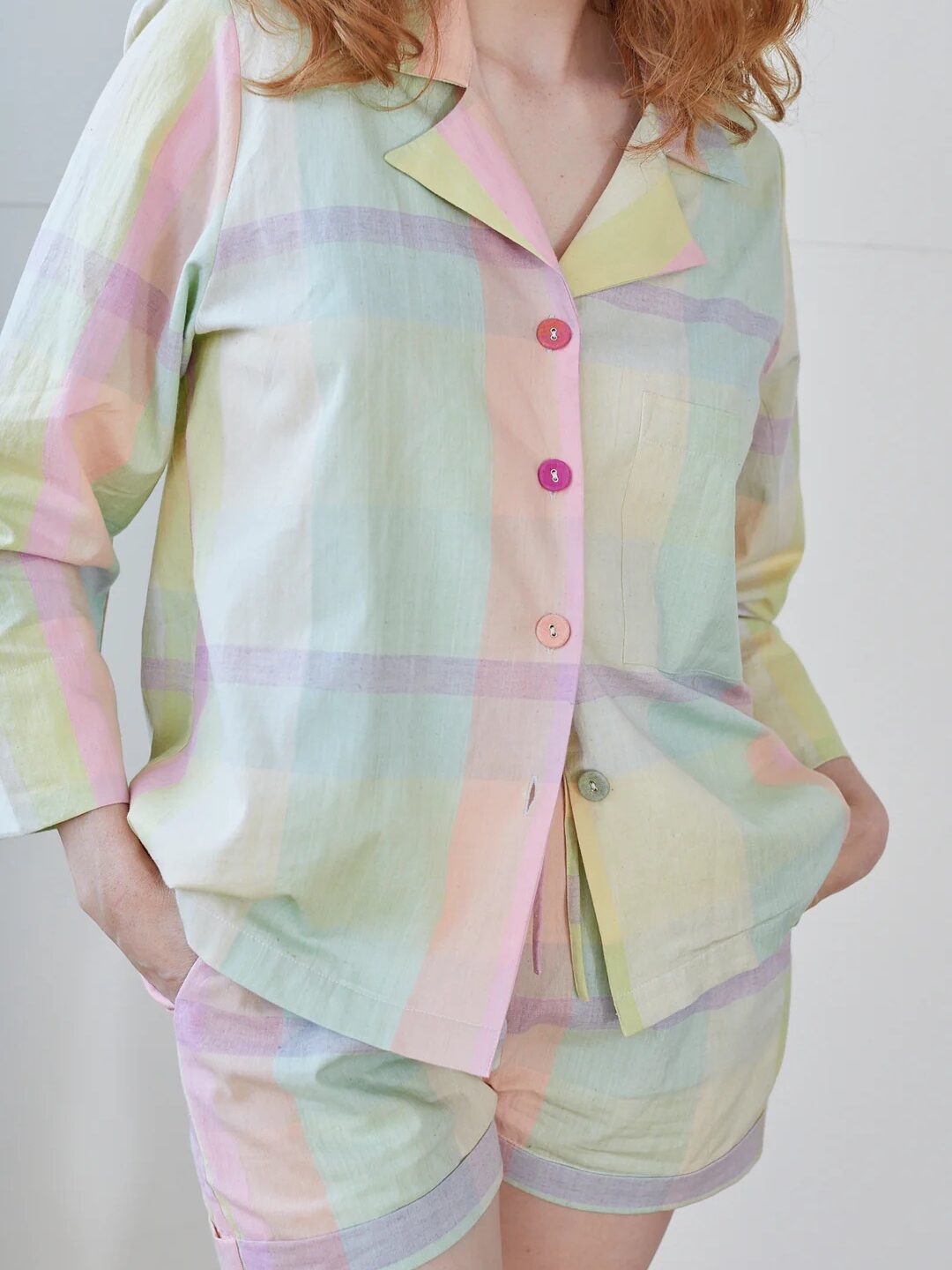 Person wearing pastel-colored plaid pajamas with one hand in the pocket of the shorts and the other by their side.