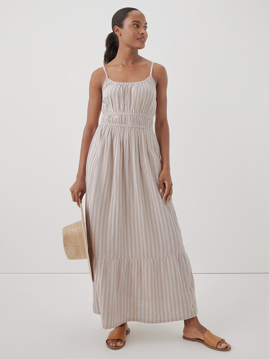 A model wearing a long beige and cream striped think strap dress from Pact. 