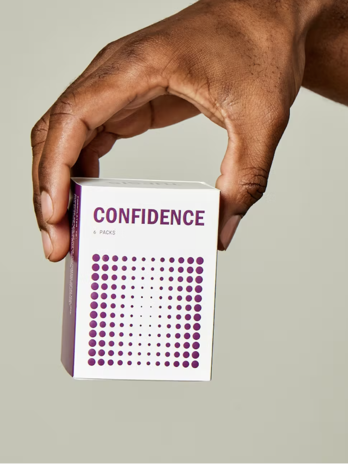 Hand holding a small white and purple box labeled "Confidence" against a plain background.