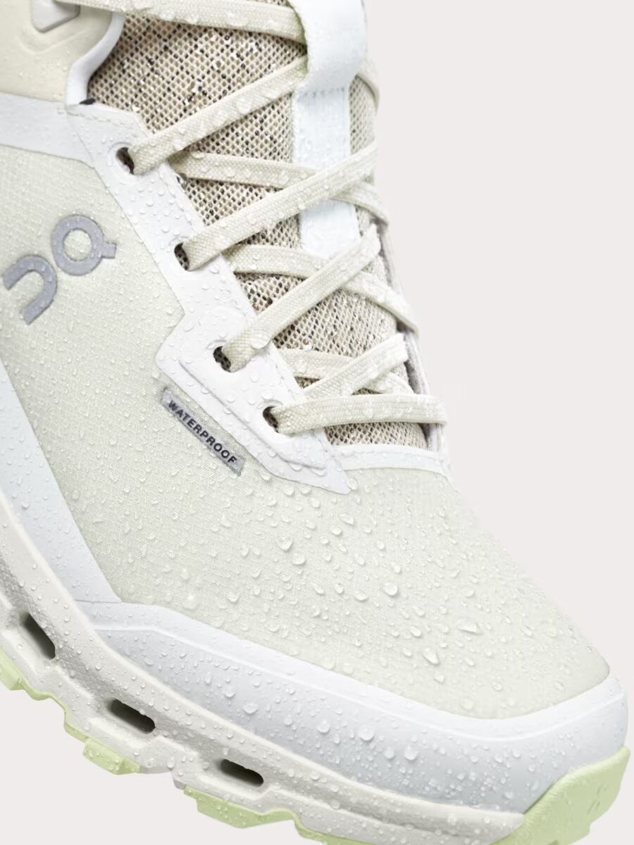 Close-up of a white waterproof athletic shoe with visible water droplets on the surface, displaying the "On" brand logo and detailed lacing.