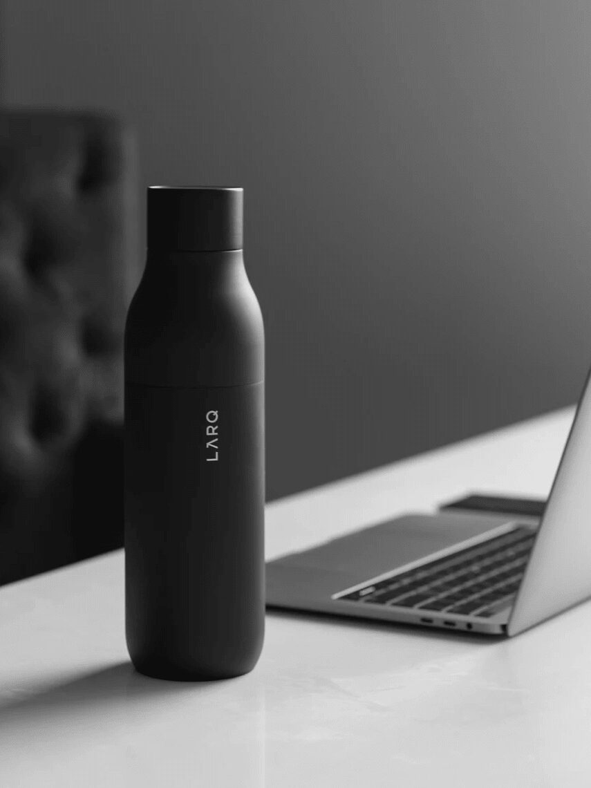 A black Larq water bottle is placed on a white desk next to an open laptop.