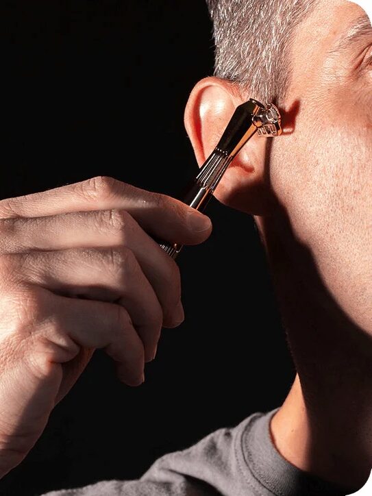 A person is touching their ear with a metal device resembling a miniature guitar.