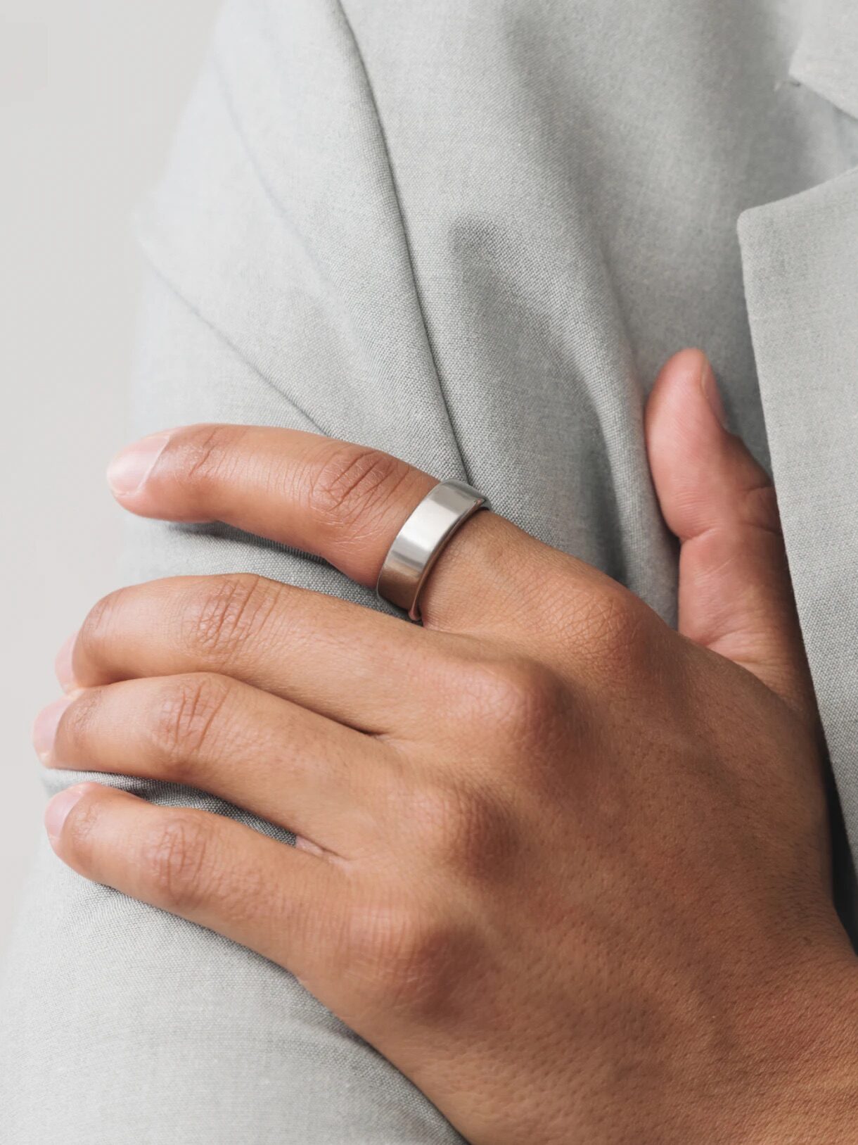 A person in a light gray suit jacket wears a silver ring on their left hand while crossing their arms.