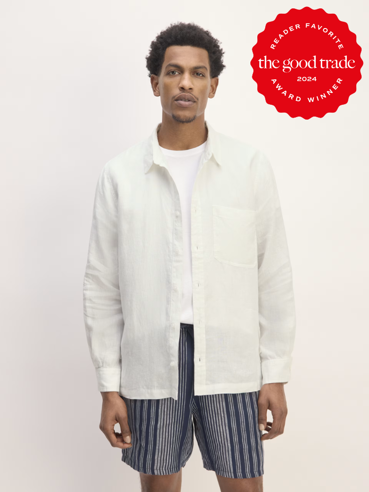 A model wearing an open button long sleeve white collared shirt with striped shorts from Everlane. 