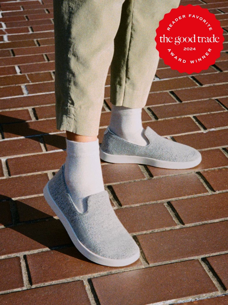 Person wearing gray slip-on shoes and light-colored socks standing on a brick pathway. A red award badge reading "the good trade Reader Favorite 2024 Award Winner" is in the upper right corner.