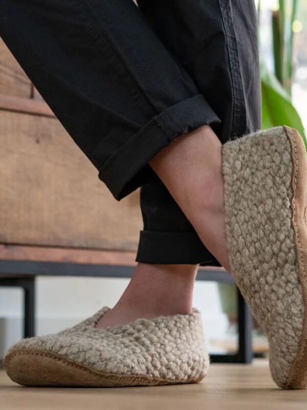 Person wearing wool slippers and black pants standing in a room with a wooden dresser.