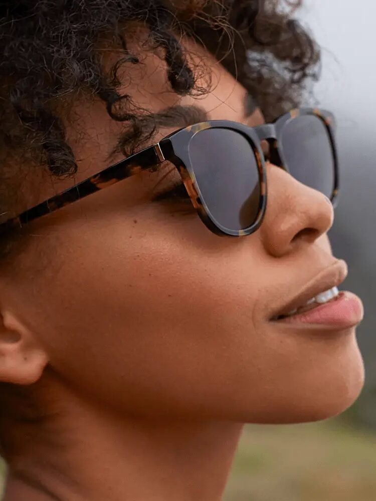 A close-up of a person wearing sunglasses and looking up, with a black space on the left side of the image.