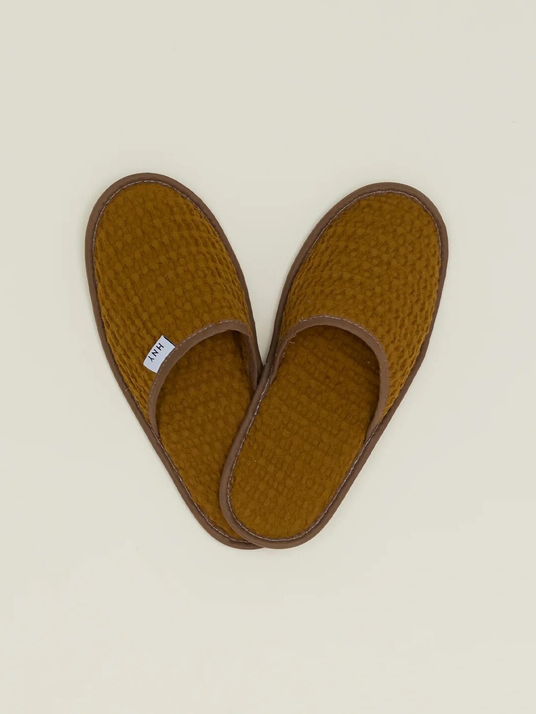 A pair of brown waffle-knit slippers with open backs, placed on a light beige background.