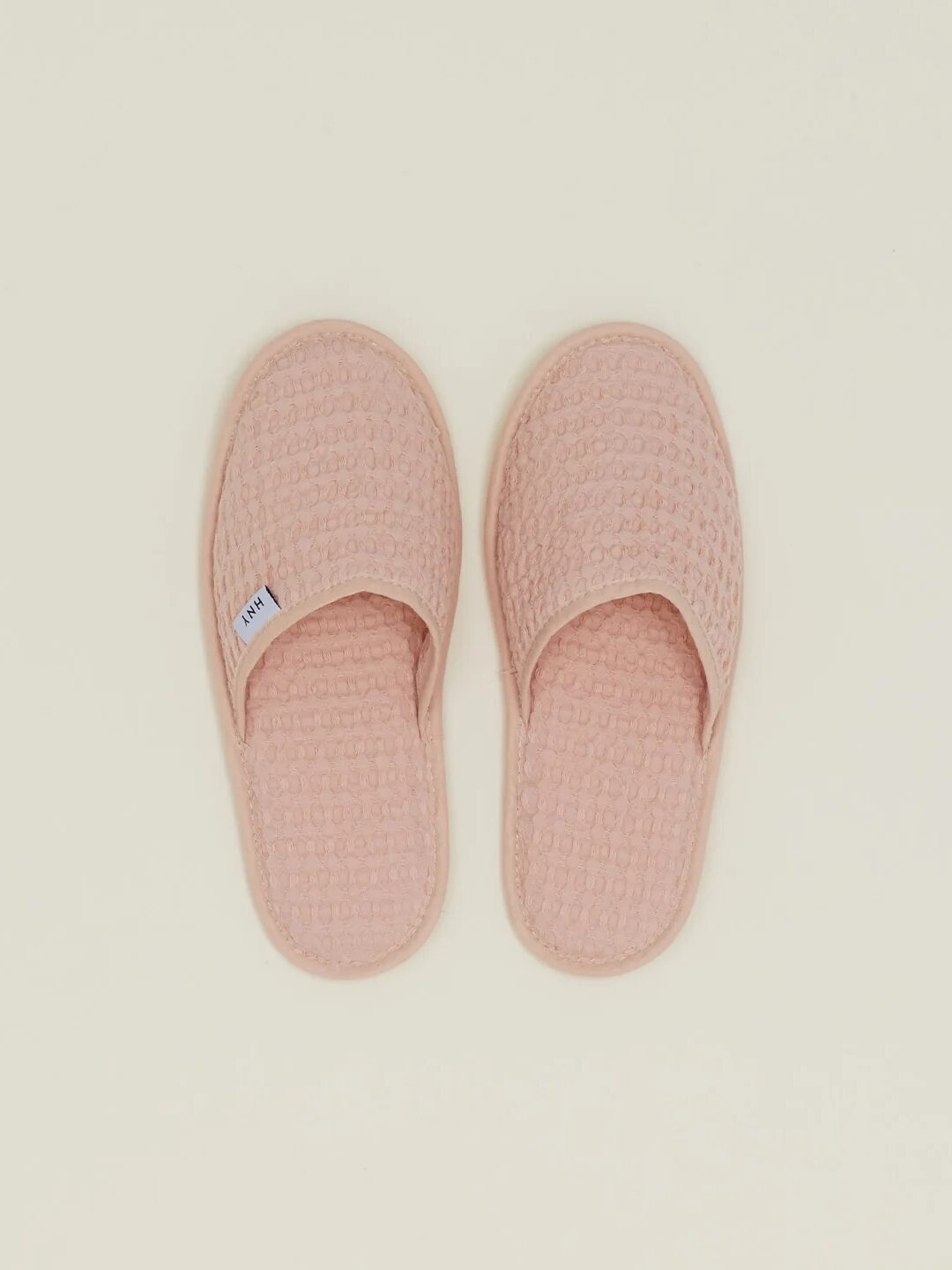 A pair of pastel pink waffle-textured slippers with open backs, placed side by side on a neutral background.