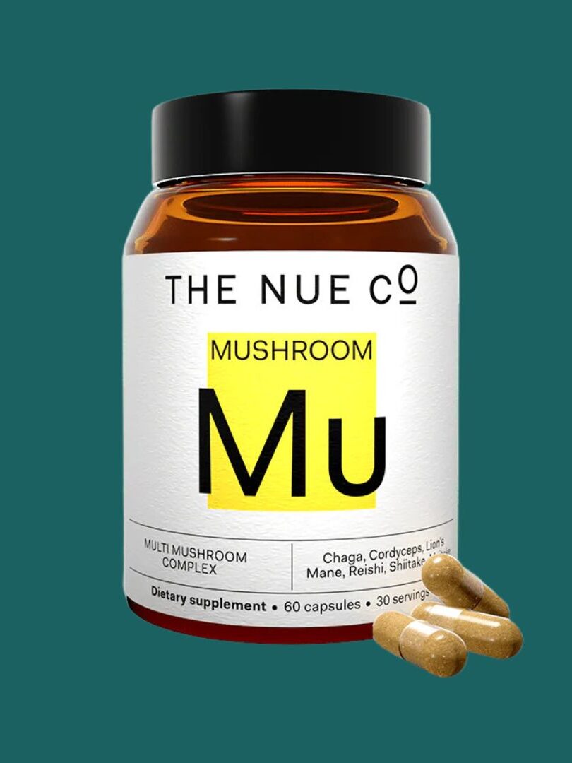 A brown jar with a black lid labeled "The Nue Co. Mushroom Mu" containing 60 capsules, with three capsules displayed outside the jar. The background is solid teal.