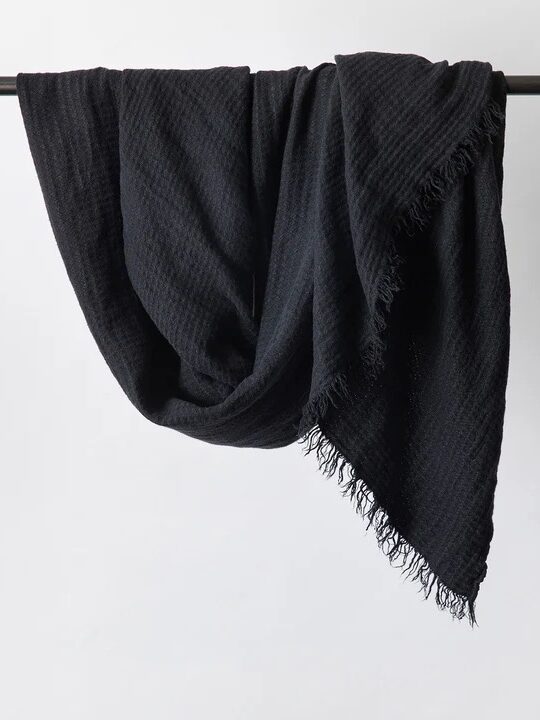 A black textured scarf with fringed edges hangs draped over a black metal bar against a plain white background.