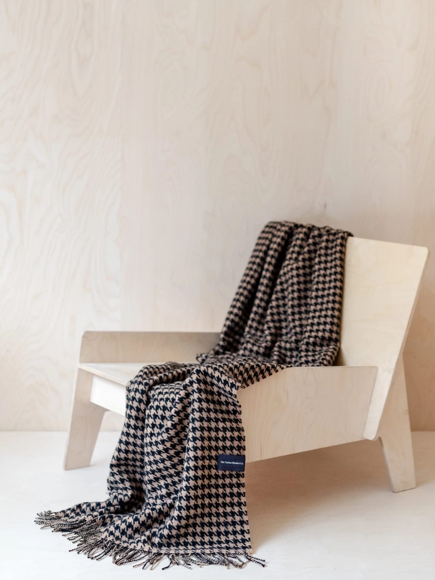 A wooden chair with a black-and-white houndstooth patterned blanket draped over it, set against a light wood-paneled wall.
