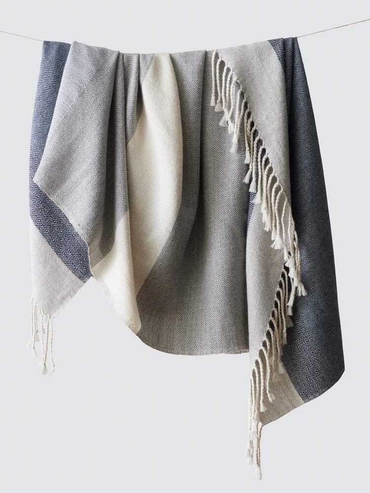A hanging multi-colored blanket with fringe, featuring black, gray, and beige sections.
